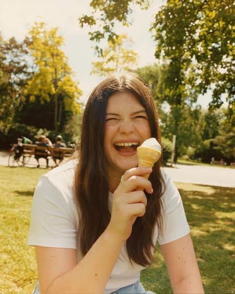 A young woman laughing in a sunny park, holding an ice cream