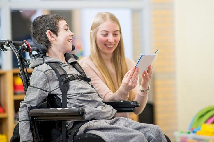 A support worker reading a book with a young boy who uses a wheelchair